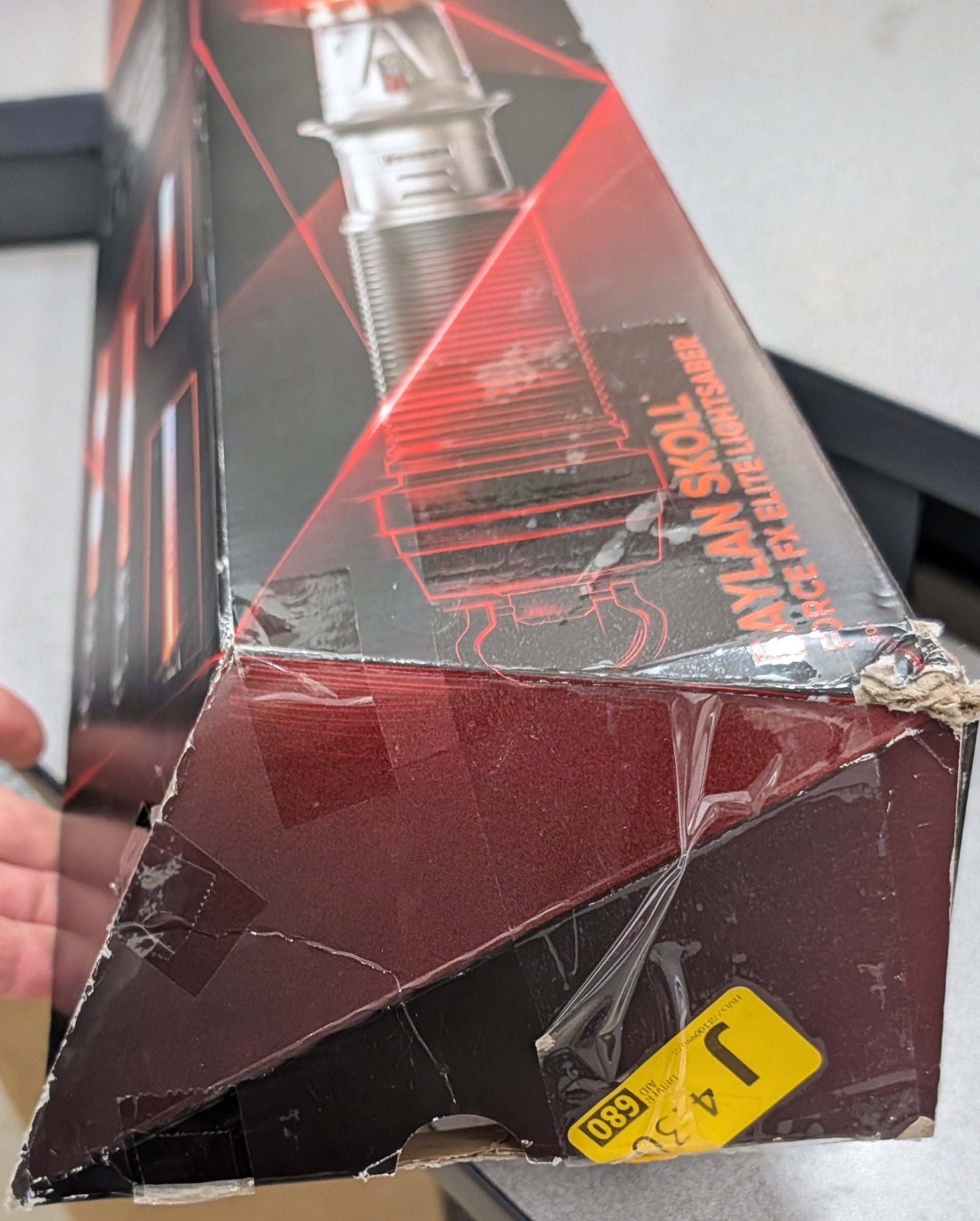 Person holding a box with a red and black design, possibly containing a product.